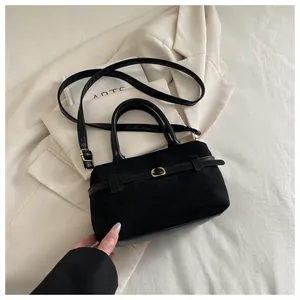 Détail du sac à main noir en daim avec sangles en cuir et boucle dorée sur blazer