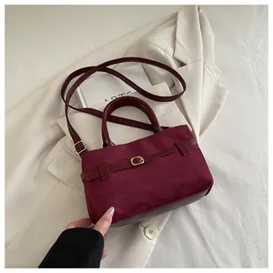 Gros plan d'un sac à main bordeaux en daim avec boucle dorée et bandoulière réglable