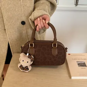 Detail of a dark brown leopard print handbag featuring a plush kitty charm on a wood table