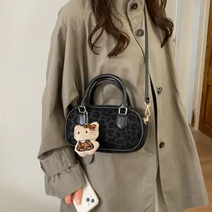 Detail of black leopard print crossbody bag with gold hardware and plush charm on trench coat
