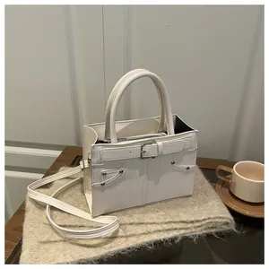 Detail shot of a cream leather handbag with decorative buckles and metal rivets