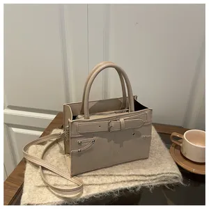 Detail of beige trapezoid handbag with buckle, metal rivets and accordion side