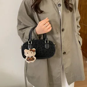 Detail view of black leopard print crossbody bag with plush charm on olive trench coat