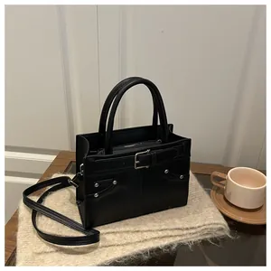 Detail of a black leather handbag with metal rivets on a plush cream fabric background