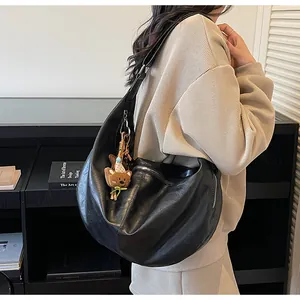 Detail view of black crescent shoulder bag with cute brown bear plush charm accessory