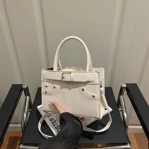 Chic off-white leather handbag with buckle strap and rivets on a stylish chair