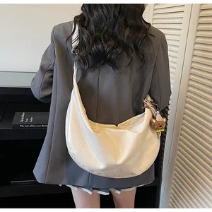 Detail of a cream hobo bag with a bear charm worn cross-body by a model in a modern room