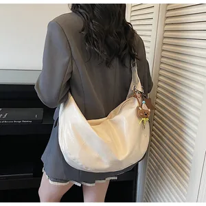 Chic beige crescent hobo bag shown on shoulder with a cute bear charm accessory