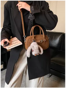 Brown leather crossbody bag with cute bunny pendant shown in a stylish lifestyle scene