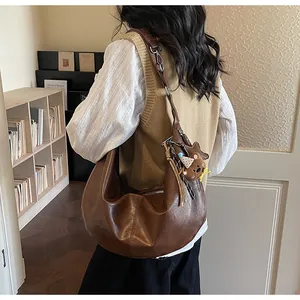 Close-up of brown crescent hobo bag with adjustable strap and cute bear pendant accessory