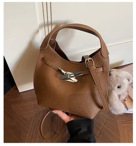 Close-up of brown lychee leather bucket bag with silver metal buckle and plush bear charm