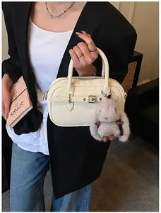 Detail of beige textured boston bag with a plush bunny charm and dual zipper closure