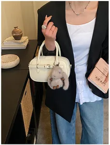 Detail of cream white small square bag with buckle and plush bunny charm on shoulder strap