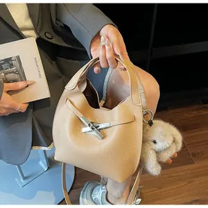 Close-up of beige lychee grain leather bucket bag with silver metal cross lock and charm