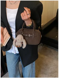 Detail of dark brown boston bag with a plush rabbit pendant and silver buckle strap
