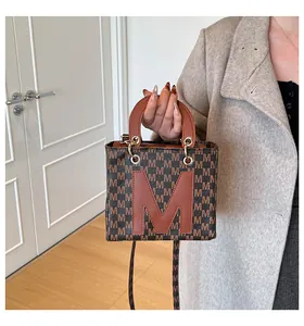 Detail of a brown monogram mini tote bag with letter M patch held by a model in a coat
