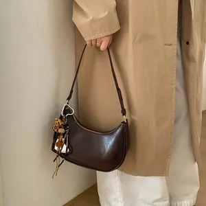Détail du sac demi-lune marron foncé avec breloques léopard sur un trench-coat beige