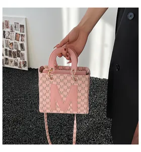 Detail of pink small square bag featuring M letter pattern and golden metal ring hardware