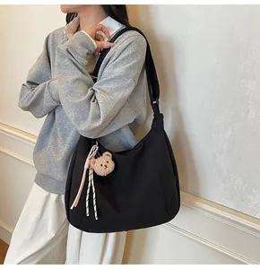 Close-up of black hobo bag with wide shoulder strap and brown plush bear charm