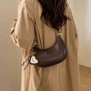 Détail d'un sac demi-lune marron foncé avec breloque cœur léopard sur un trench-coat