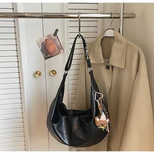 Detail of black leather crescent hobo bag with adjustable strap and cute bear charm