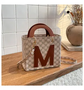 Close-up of beige handbag featuring textured M letter print and gold metal hardware hooks