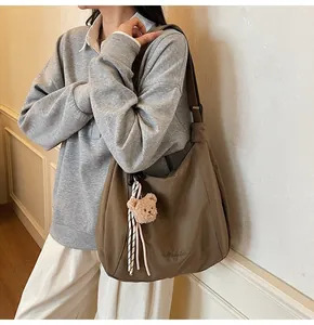 Detailed view of brown canvas tote bag with shoulder strap and plush bear charm accessory