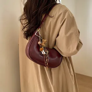 Détail du sac à bandoulière croissant rouge foncé avec manteau beige et breloque léopard