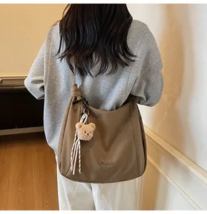Detail view of large dark brown canvas tote bag with embroidery and bear pendant charm