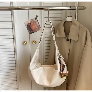 Detail of a creamy white oversized crescent hobo bag featuring a cute brown bear charm