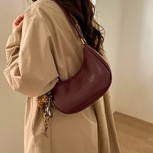 Sac croissant bordeaux en cuir avec breloque léopard porté sur un trench-coat