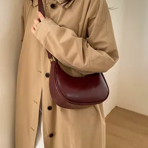 Sac croissant en cuir verni bordeaux porté avec un trench-coat kaki pour un style rétro chic