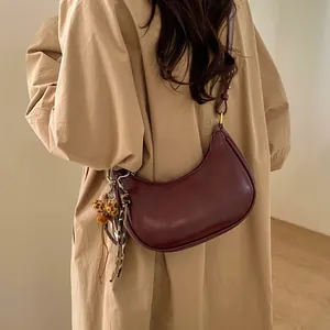 Détail du sac demi-lune bordeaux avec foulard léopard et charm peluche sur trench-coat