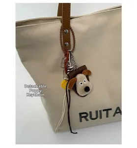 Detail van beige canvas tas met lederen handvat en een afneembare pluche honden hanger