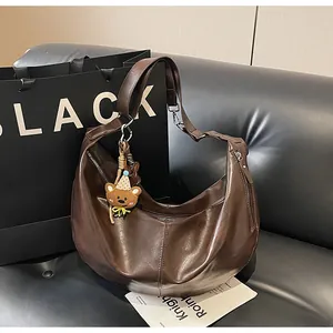 Detail view of a dark brown crescent leather bag on a sofa with a bear charm