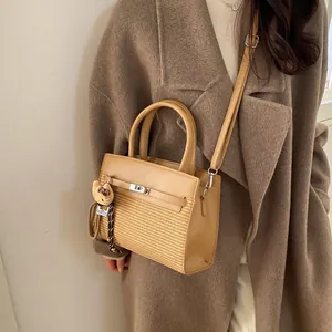 Chic beige patchwork handbag with straw texture and cat charm on a wool coat model