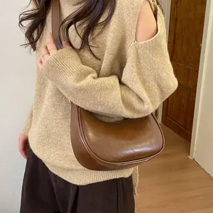 Détail d'un sac hobo croissant marron foncé en similicuir brillant porté à l'épaule