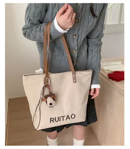 Détail du sac cabas en toile avec anses brunes, broderie RUITAO et breloque chien