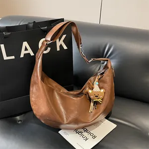 Brown leather crescent bag with bear charm on leather couch with fashion accessories