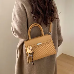 Detail of a brown patchwork handbag with woven texture and a plush charm on a long coat