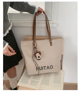 Vue détaillée du sac cabas en toile beige avec sangles marron et pendentif peluche