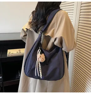 Detail of dark blue nylon hobo bag with teddy bear pendant worn on model shoulder