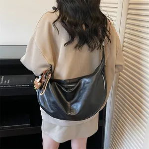Minimalist black crescent crossbody bag with plush bear charm in urban casual setting