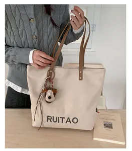 Détail du sac fourre-tout en toile blanc cassé avec anses brunes et breloque chien en peluche