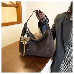 Detail of a large brown suede hobo bag with a silver zipper and cute bear pendant