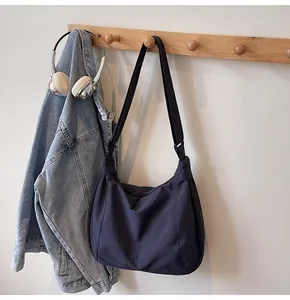 Detail of a navy nylon crossbody bag hanging with a denim jacket and headphones