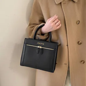 Détail du sac à main noir texturé avec ferrures dorées et double zip sur le manteau