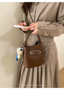 Detail of dark brown lychee leather bucket bag with silver buckle and plush bear charm