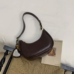 Sac croissant marron foncé avec miroir cœur léopard posé sur une chaise tressée
