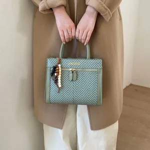 Détail du sac à main vert à chevrons avec breloque en bois et logo doré élégant